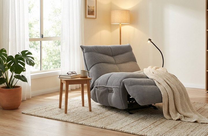 Gray recliner chair in a cozy living room with a blanket and small table.